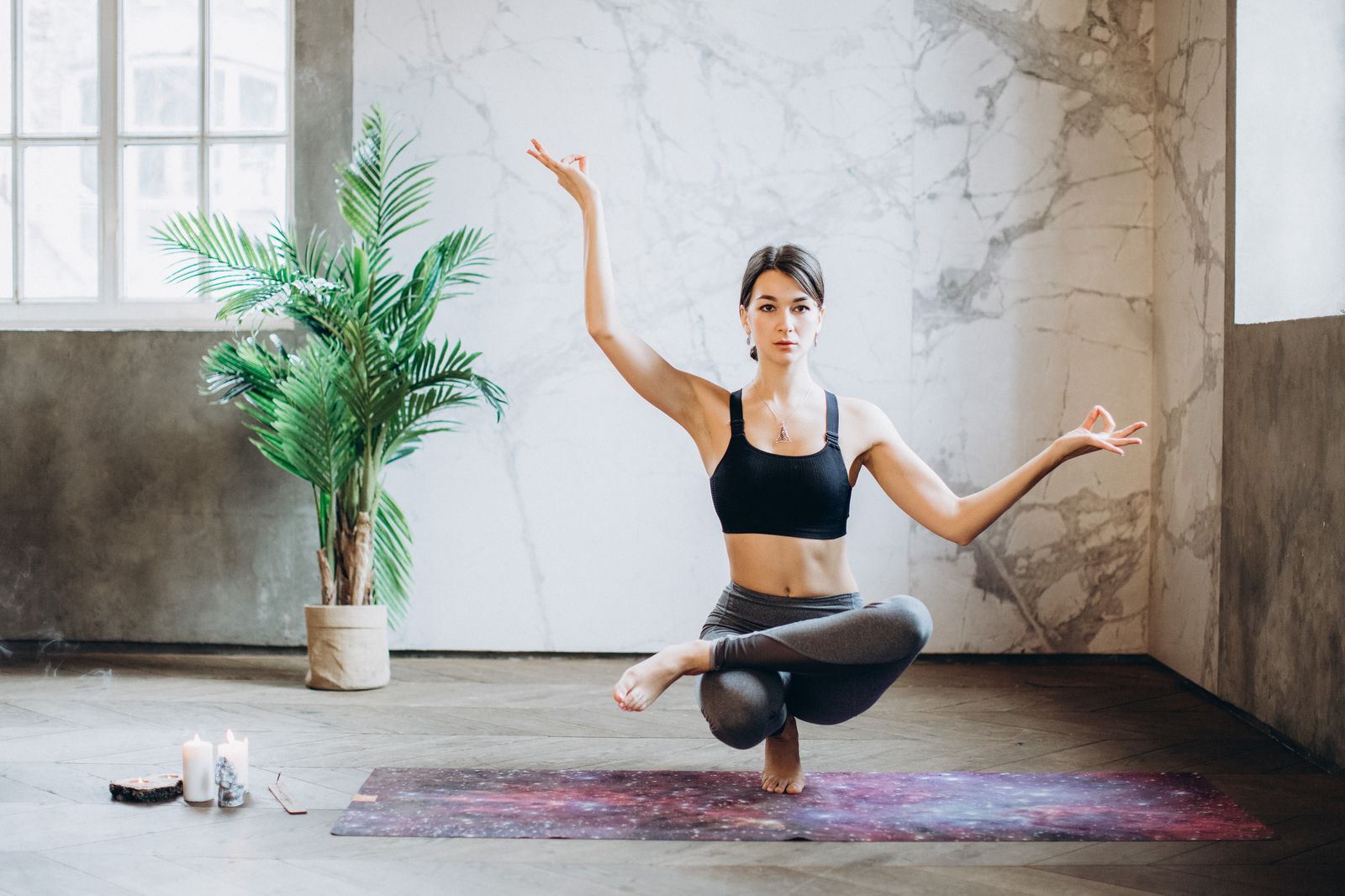 An instructor holding a one-legged balance in a bright loft studio — a class paused mid-practice in the member player