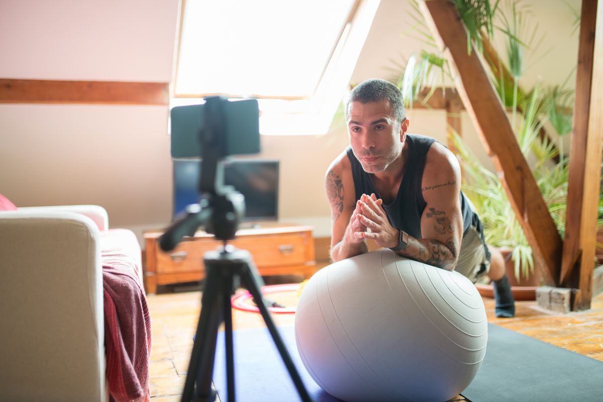 Coach filming an exercise-ball workout at home with a phone on a tripod