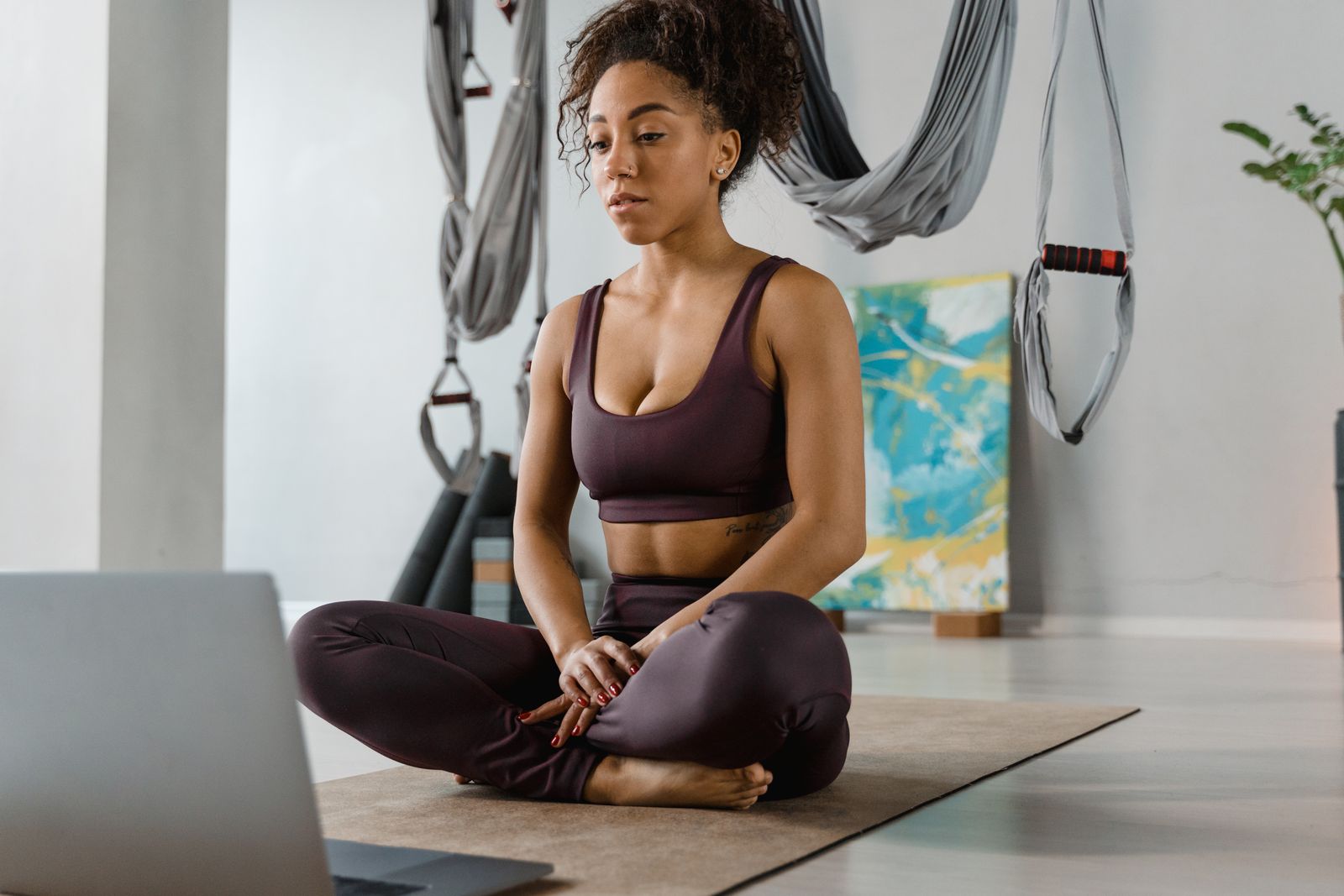 Pilates instructor sitting cross-legged in a studio reviewing numbers on a laptop