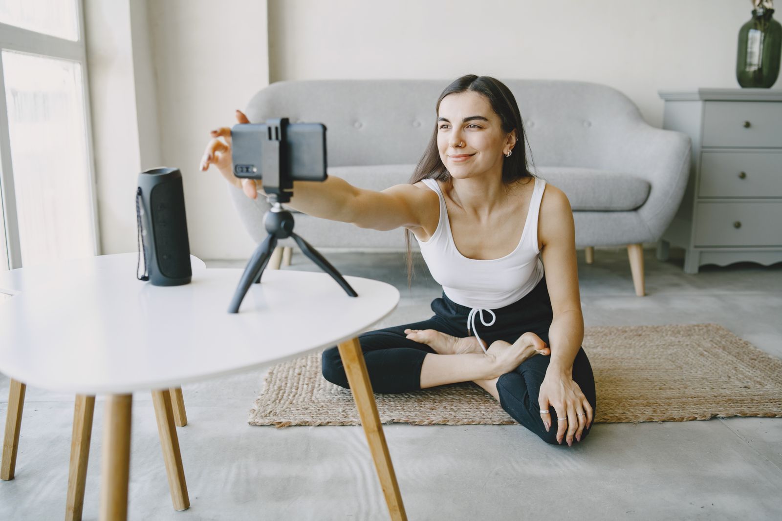 Yoga teacher adjusting a phone on a small tripod before recording a class at home
